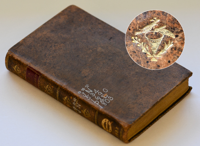 livre relié en cuir brun couché sur une surface blanche, cercle avec plan rapproché de dorures